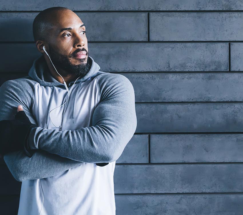 Black male standing in front of brick wall listening to music